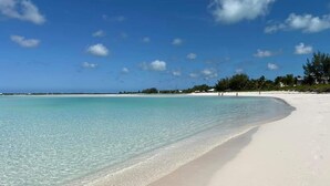 A beach with clear turquoise water, white sand, and a few people walking along the shore. - Sandy & Salty Beach Cottage (Spanish Wells)
