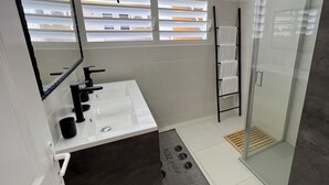 A modern bathroom with a white sink, black faucet, and a glass shower enclosure. - VILLA PHARE CARAIBES (Le Moule)
