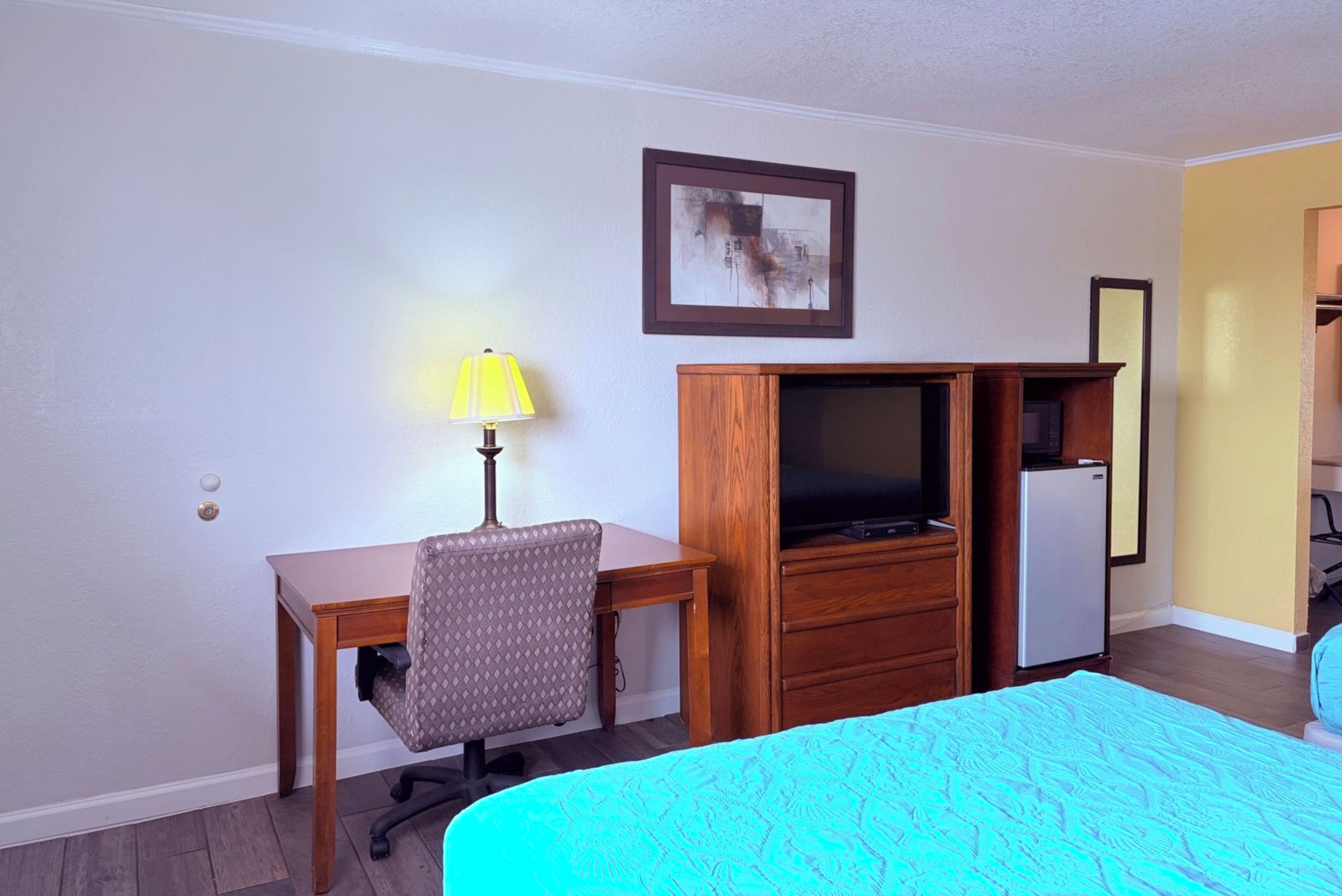 Quarto de hotel com uma cama, uma escrivaninha com cadeira, televisão e frigorífico.
