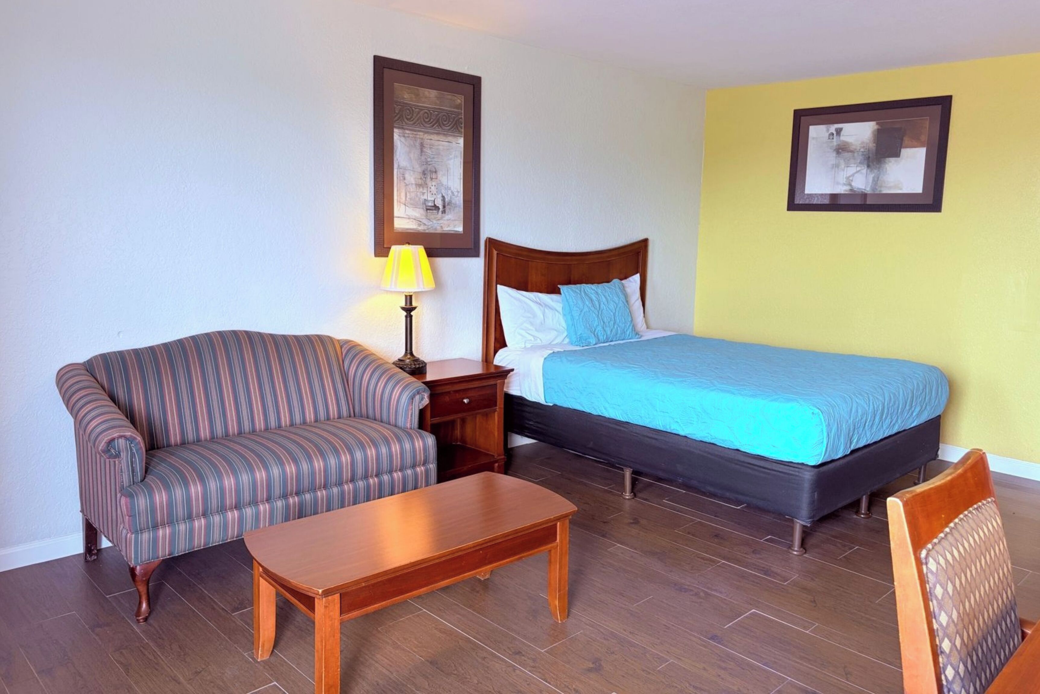 A hotel room with a bed, a sofa, a wooden table, and a lamp.