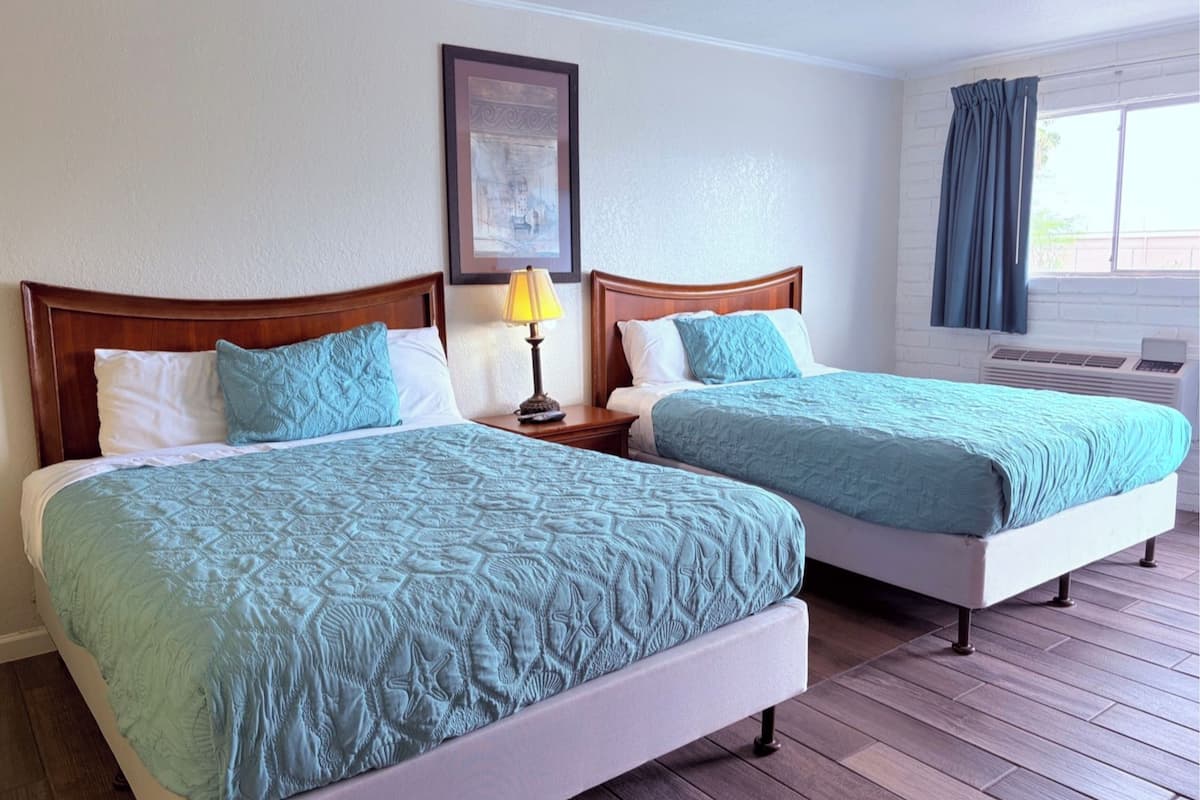 Two beds with matching headboards, a bedside table with a lamp, a framed picture on the wall, and a window with curtains.
