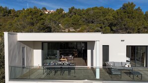 A modern house with a glass balcony, a dining area with a table set for four, and a view of the surrounding forest.