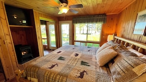 A wooden cabin bedroom with a bed, a fireplace, and a ceiling fan.