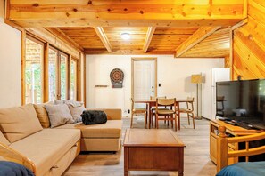 A cozy living room with a sofa, a coffee table, a TV, and a dining area with chairs and a table. - Spacious Chalet with Game Loft & Pool Access (Arnold)