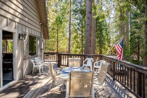 A wooden deck with outdoor furniture, a flag, and a view of a forest. - Spacious Chalet with Game Loft & Pool Access (Arnold)