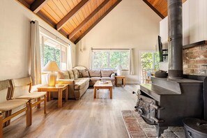 A cozy living room with a fireplace, wooden furniture, and large windows. - Spacious Chalet with Game Loft & Pool Access (Arnold)