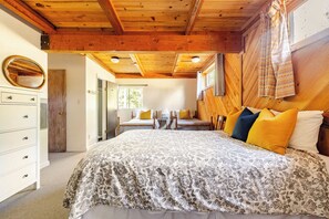 Une chambre avec un plafond en bois, un lit recouvert d’une literie à motifs floraux, une table de chevet et un miroir.