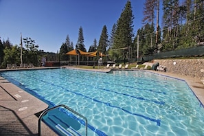 A swimming pool with clear blue water, surrounded by a stone wall and trees. - Spacious Chalet with Game Loft & Pool Access (Arnold)