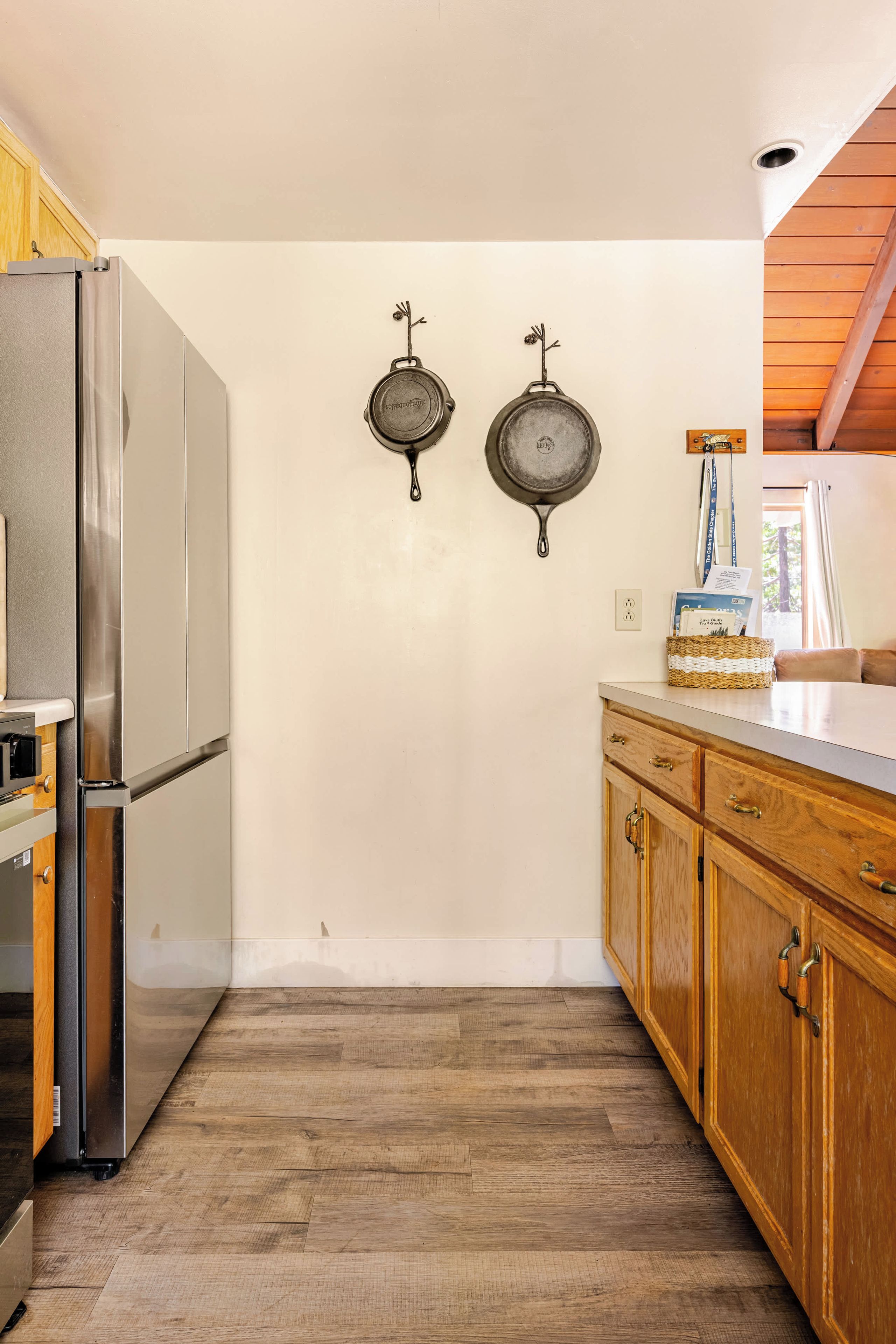 Een keuken met houten kastjes, een roestvrijstalen koelkast en twee hangende pannen.