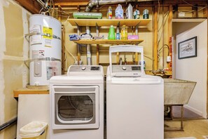 A laundry area with stacked dryers, a water heater, and various cleaning supplies on shelves. - Spacious Chalet with Game Loft & Pool Access (Arnold)