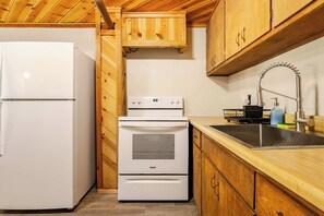 A compact kitchen with a refrigerator, stove, and sink, wooden cabinets, and a wooden ceiling. - Spacious Chalet with Game Loft & Pool Access (Arnold)
