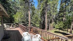 Eine Holzterrasse mit einem Glastisch und Stühlen, umgeben von hohen Bäumen.