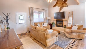 Ein Wohnzimmer mit zwei beigefarbenen Sofas, einem Holztisch, einem Fernseher, einem Kamin und einem Deckenventilator.