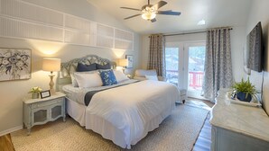 Ein Schlafzimmer mit einem großen Bett, einem Deckenventilator, einem Nachttisch mit Lampe, einem Schminktisch und einem Fenster mit Vorhängen.