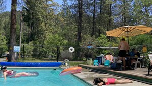Une piscine avec des bouées gonflables, un espace ombragé et une terrasse entourée d’une clôture.