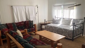 Une pièce comprenant un ensemble de meubles de salon en bois, un lit avec une literie à motifs, une petite table et une lampe sur pied.