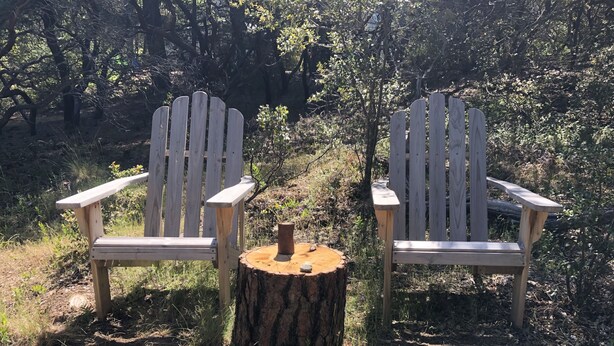 Deux fauteuils Adirondack, séparés par un tronc d’arbre, dans un cadre naturel.