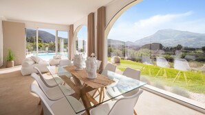 A modern dining area with a glass table, white chairs, and a view of a pool and mountains. - Curina Luxury Villa - design pool villa in Scopello (Castellammare del Golfo)