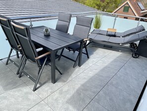 A rooftop terrace with a dining table and chairs, a small potted plant, and a glass balustrade. - Windward: New, Modern Apartment Near the Beach *Wallbox* (Wurster Nordseeküste)