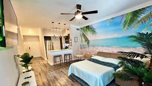 Un dormitorio con una cama, un escritorio, una silla, un ventilador de techo y un mural de playa.