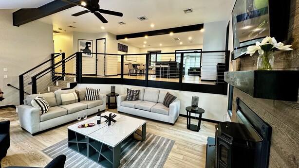 Un salón espacioso con un sofá grande, una mesa de centro y una chimenea. Se ve una escalera que conduce a un nivel superior con comedor.