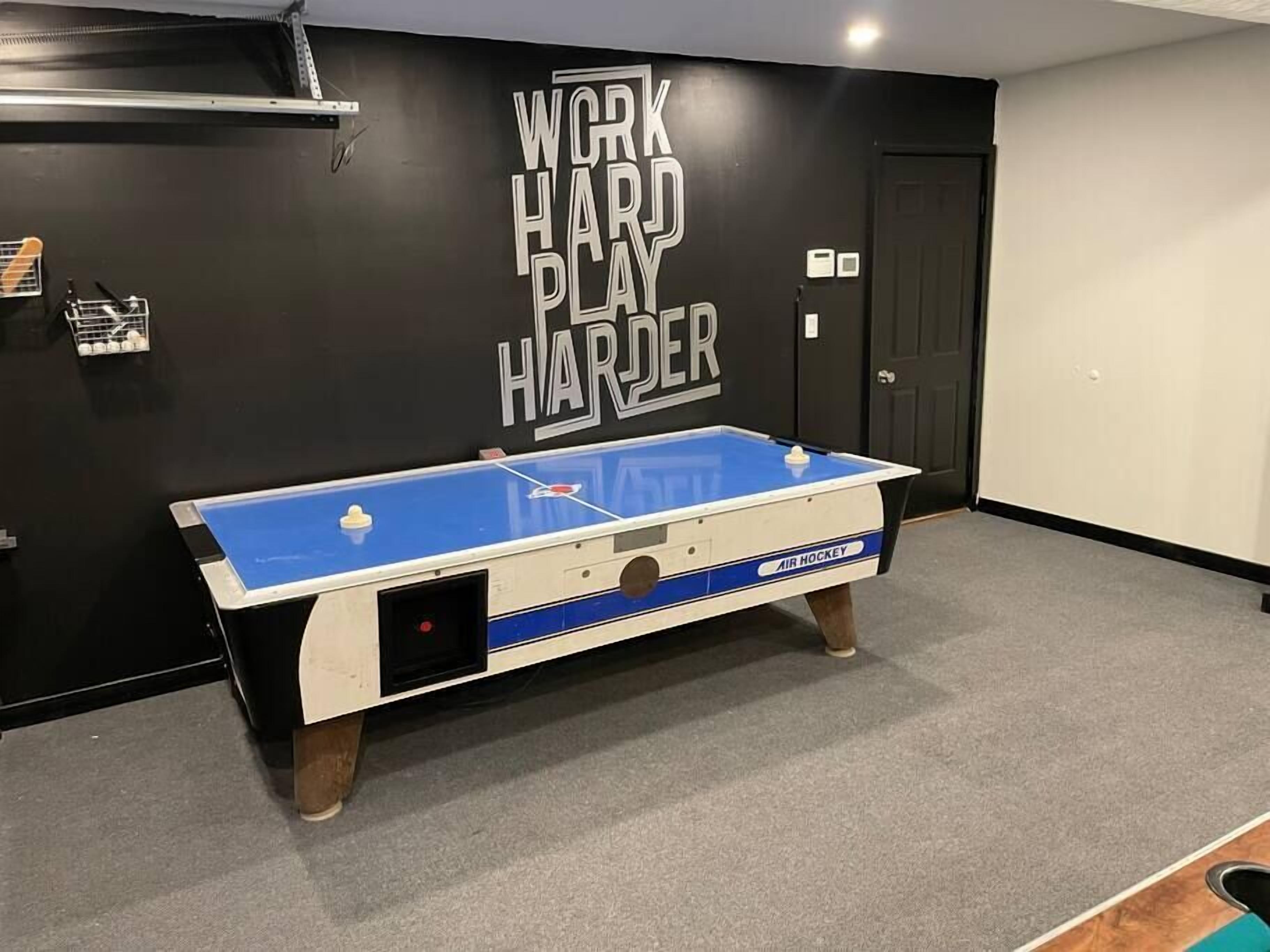 A pool table in a room with a black wall featuring the text "WORK HARD PLAY HARDER".