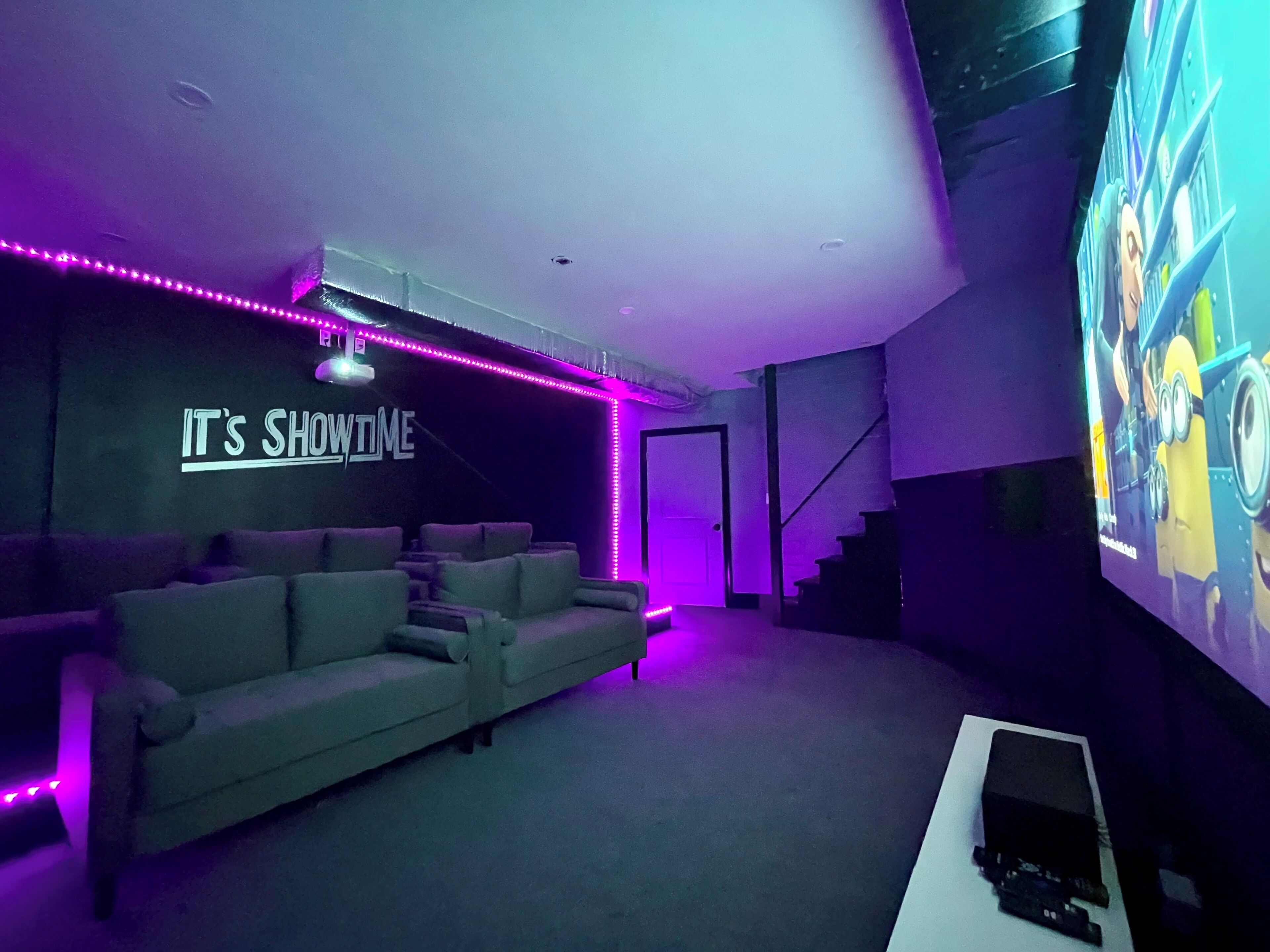 A home theater room with a couch, a large screen, and purple LED lights.