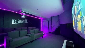 A home theater room with a couch, a large screen, and purple LED lights.