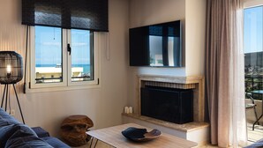 A modern living room with a fireplace, a flat-screen TV, and a view of the sea.