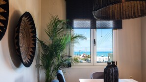 A dining area with a view of the sea, a large plant, and two vases on a table.