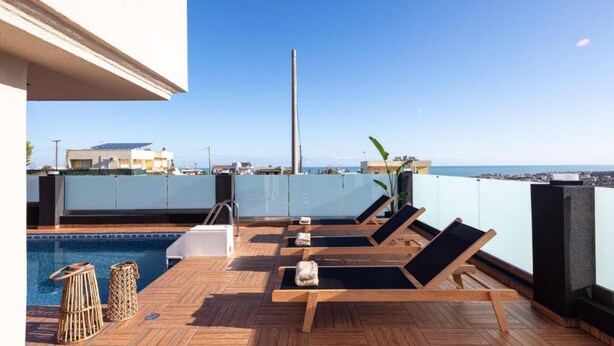 A rooftop pool area with wooden loungers and a view of the sea.