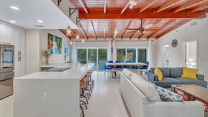 A modern kitchen with white cabinetry, a large island, and a dining area with blue chairs and a gray sofa. - Hidden Getaway Pool Home on 1.5 acres near all. Sleeps 17. Pool, ping pong etc. (Fort Lauderdale)