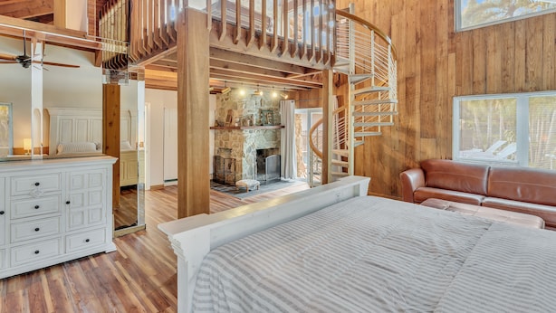A spacious bedroom with a large bed, a wooden staircase, and a stone fireplace. - Hidden Getaway Pool Home on 1.5 acres near all. Sleeps 17. Pool, ping pong etc. (Fort Lauderdale)