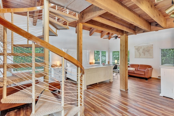 A spacious room with a wooden staircase, a bed, a white cabinet, and a leather sofa.