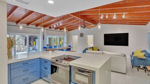 A modern kitchen with a central island, built-in ovens, and a dining area with blue chairs. - Hidden Getaway Pool Home on 1.5 acres near all. Sleeps 17. Pool, ping pong etc. (Fort Lauderdale)