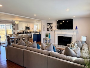 A modern living room with a sectional sofa, a fireplace, a TV, and a kitchen in the background.