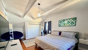Quarto com cama, escrivaninha, cadeira, ventoinha no teto e obra de arte na parede.