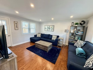 A living room with a dark blue sofa, a wooden coffee table, and a bookshelf with books and decorative items.