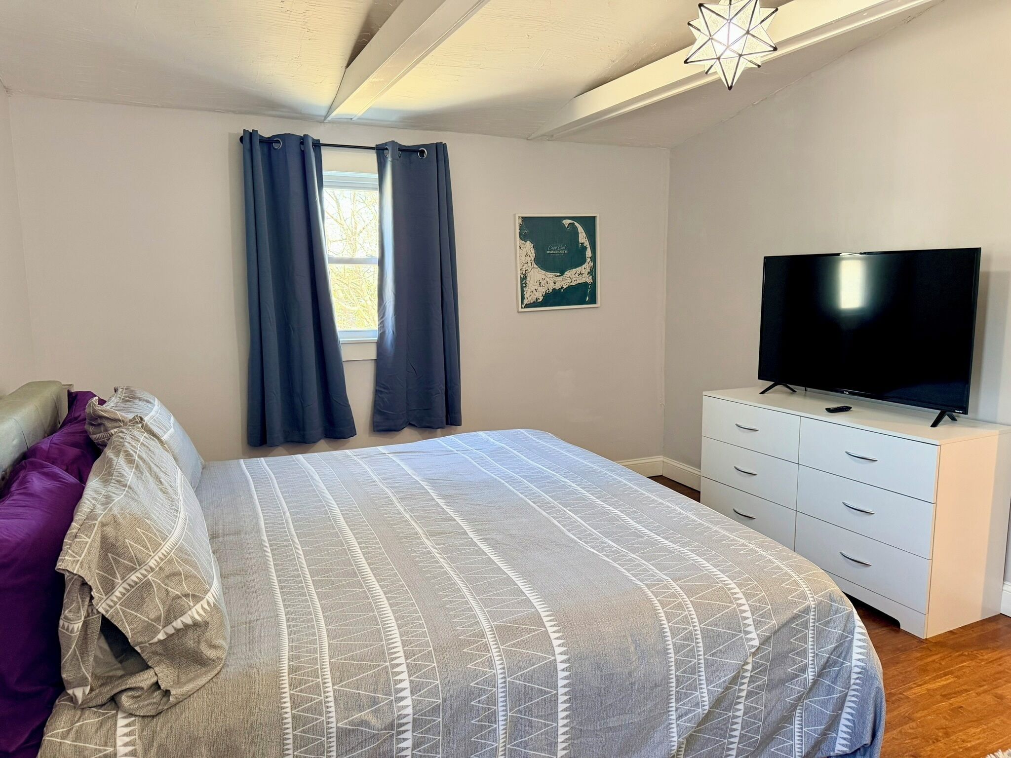 A bedroom with a bed, a dresser, a television, and a window with curtains.