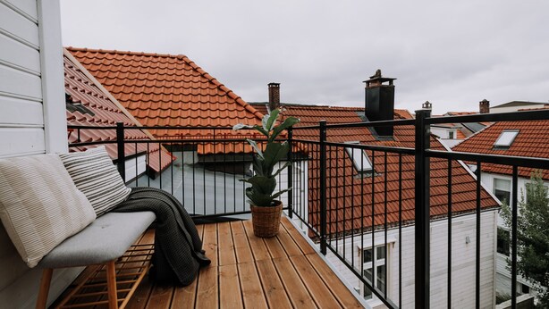 A wooden deck with a bench and a potted plant, overlooking a neighborhood with red-tiled roofs. - Bergen Beds - The Penthouse (Bergen)