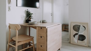 A minimalist room with a wooden desk, a chair, a flat-screen TV mounted on the wall, and a framed abstract artwork on the wall. - Bergen Beds - The Penthouse (Bergen)