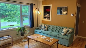 Una sala de estar con un sofá verde, una mesa de centro de madera y una ventana con cortinas.