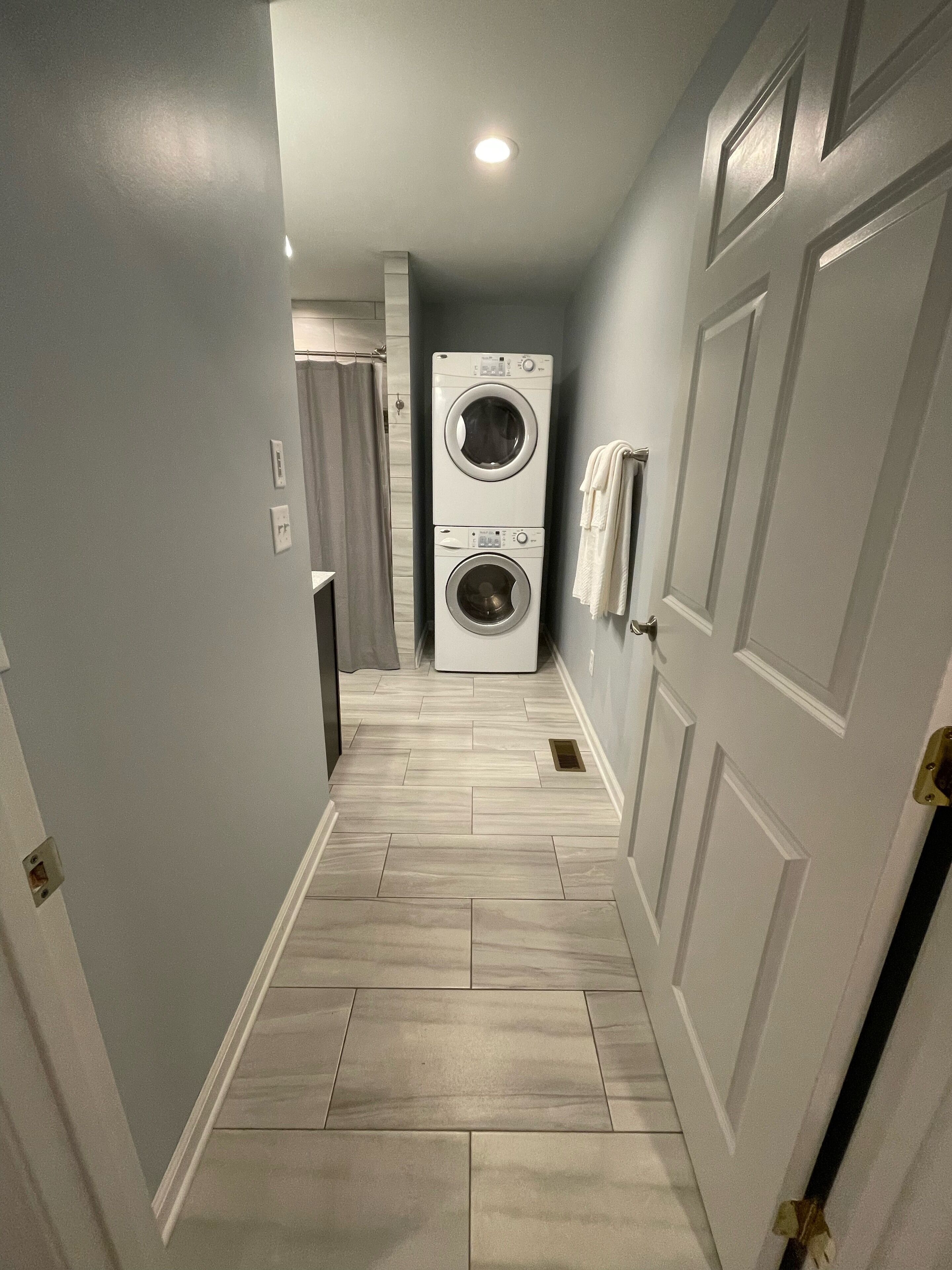 A laundry room with two stacked washing machines, a shower area, and a tiled floor.