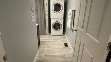 A laundry room with two stacked washing machines, a shower area, and a tiled floor.