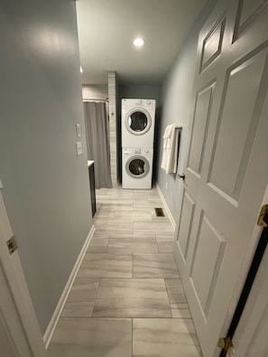 A laundry room with two stacked washing machines, a shower area, and a tiled floor.