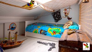 Ein Kinderzimmer im Piratendesign, mit einem Schiffmodell, einer Reckschaukel und einem Bett mit einer Weltkarte.