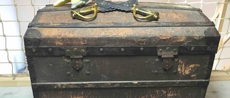 A vintage-style trunk with metal latches and brass handles, placed against a tiled wall.