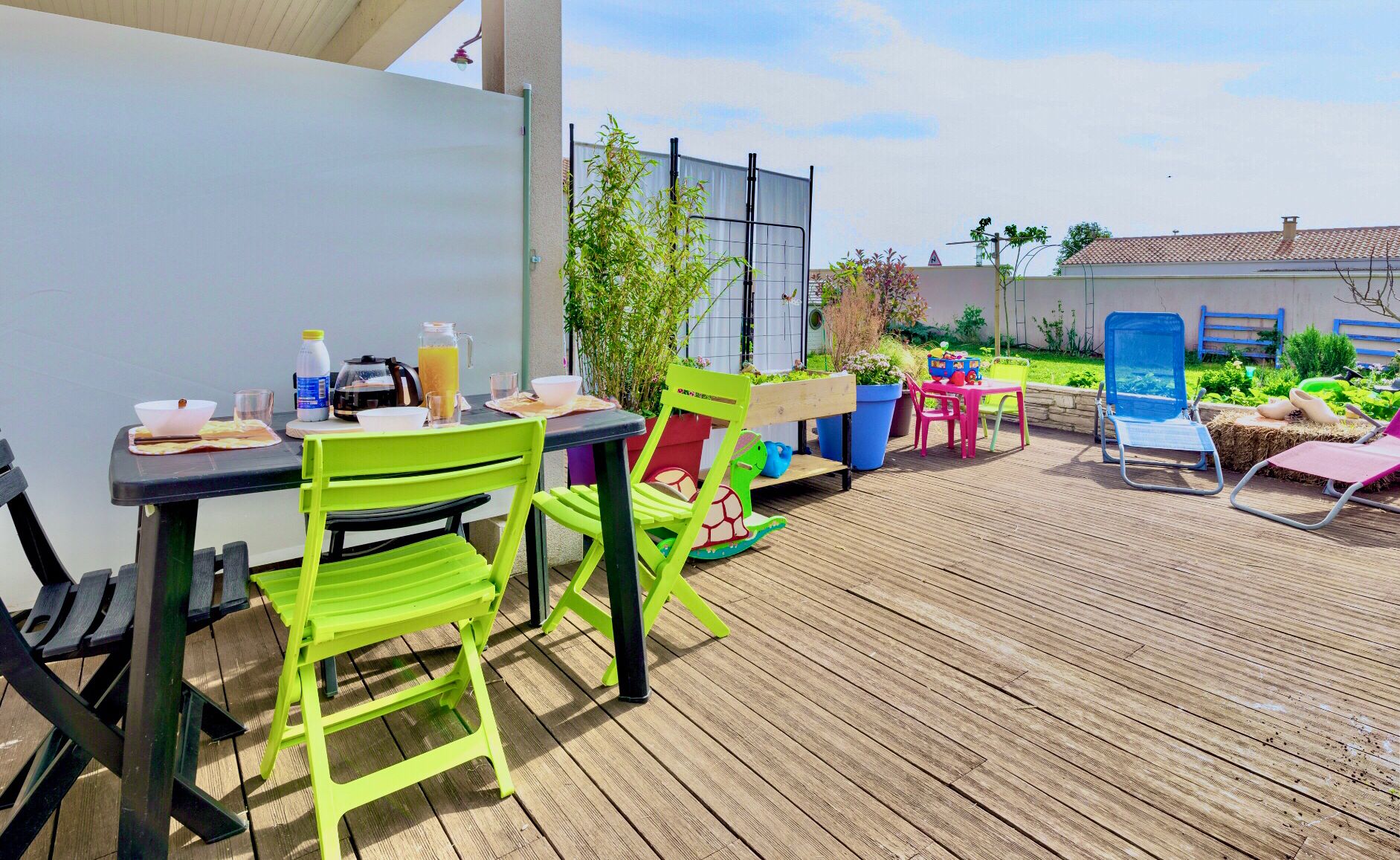 Een buitenpatio met een tafel en stoelen, een houten terras en een tuin.
