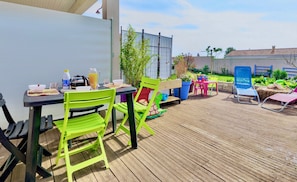 En udendørs terrasse med bord og stole, en træterrasse og en have.