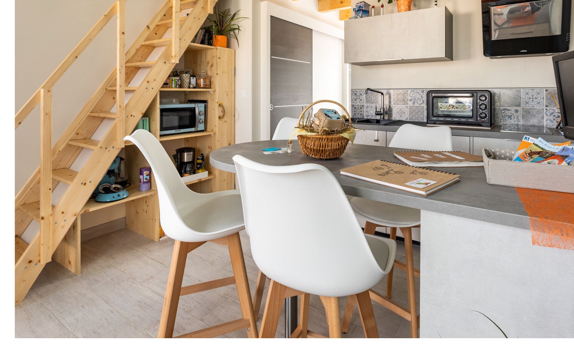 A modern kitchen with a built-in microwave, a large island with seating, and a wooden staircase leading to a loft area.